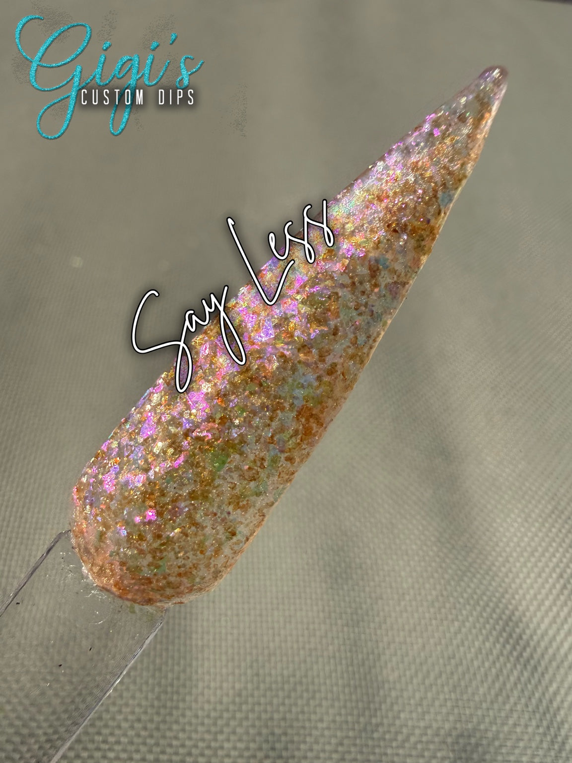 Labeled Say Less translucent pearl dip powder swatch with pink, lilac, champagne gold, aqua and pale green iridescent flakes