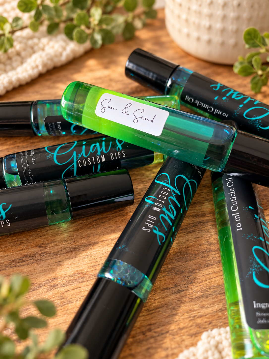 Styled product photo of Sun & Sand Cuticle Roller cuticle oil with warm wood, greenery, and cream accents