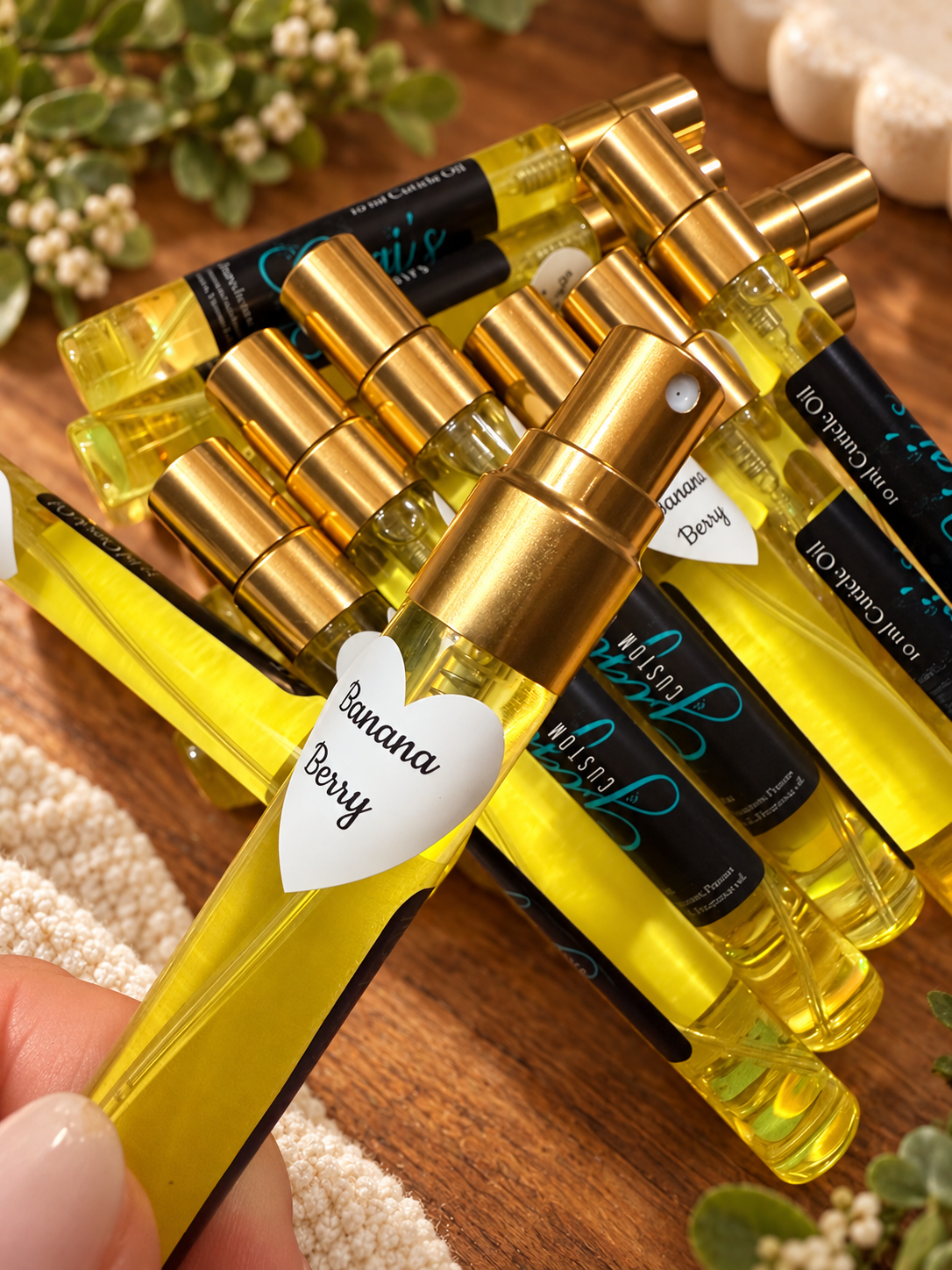 Styled product photo of Banana Berry Cuticle Oil Spray cuticle oil with warm wood, greenery, and cream accents