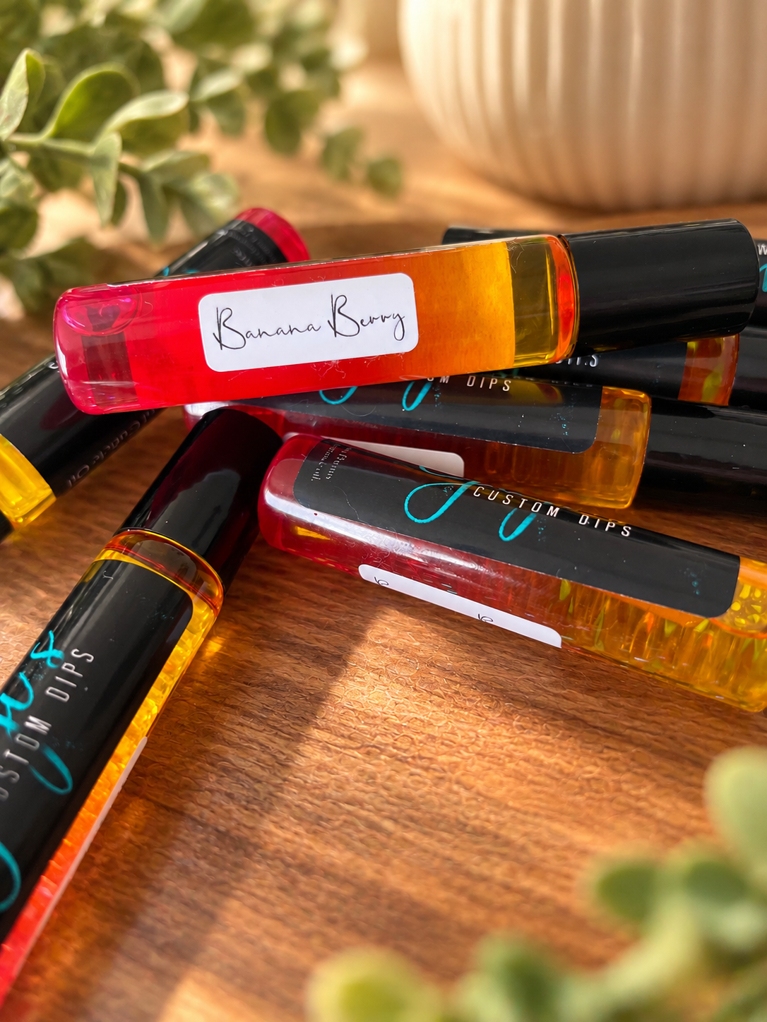 Styled product photo of Banana Berry Cuticle Roller cuticle oil with warm wood, greenery, and cream accents
