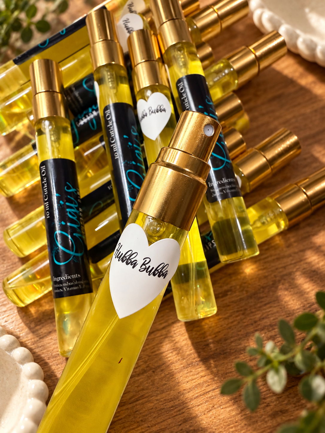Styled product photo of Hubba Bubba Cuticle Oil Spray cuticle oil with warm wood, greenery, and cream accents