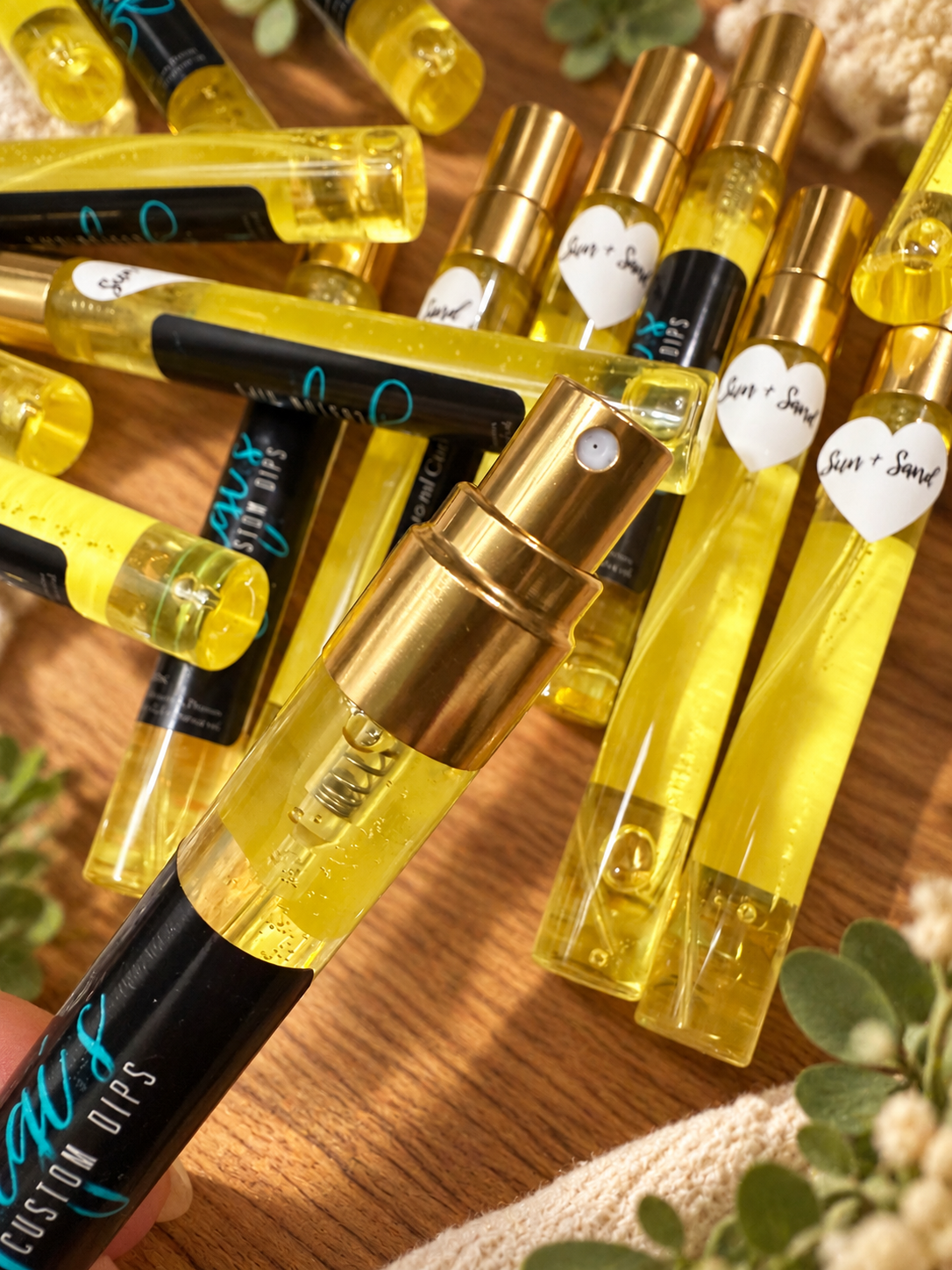 Styled product photo of Sun & Sand Cuticle Oil Spray cuticle oil with warm wood, greenery, and cream accents