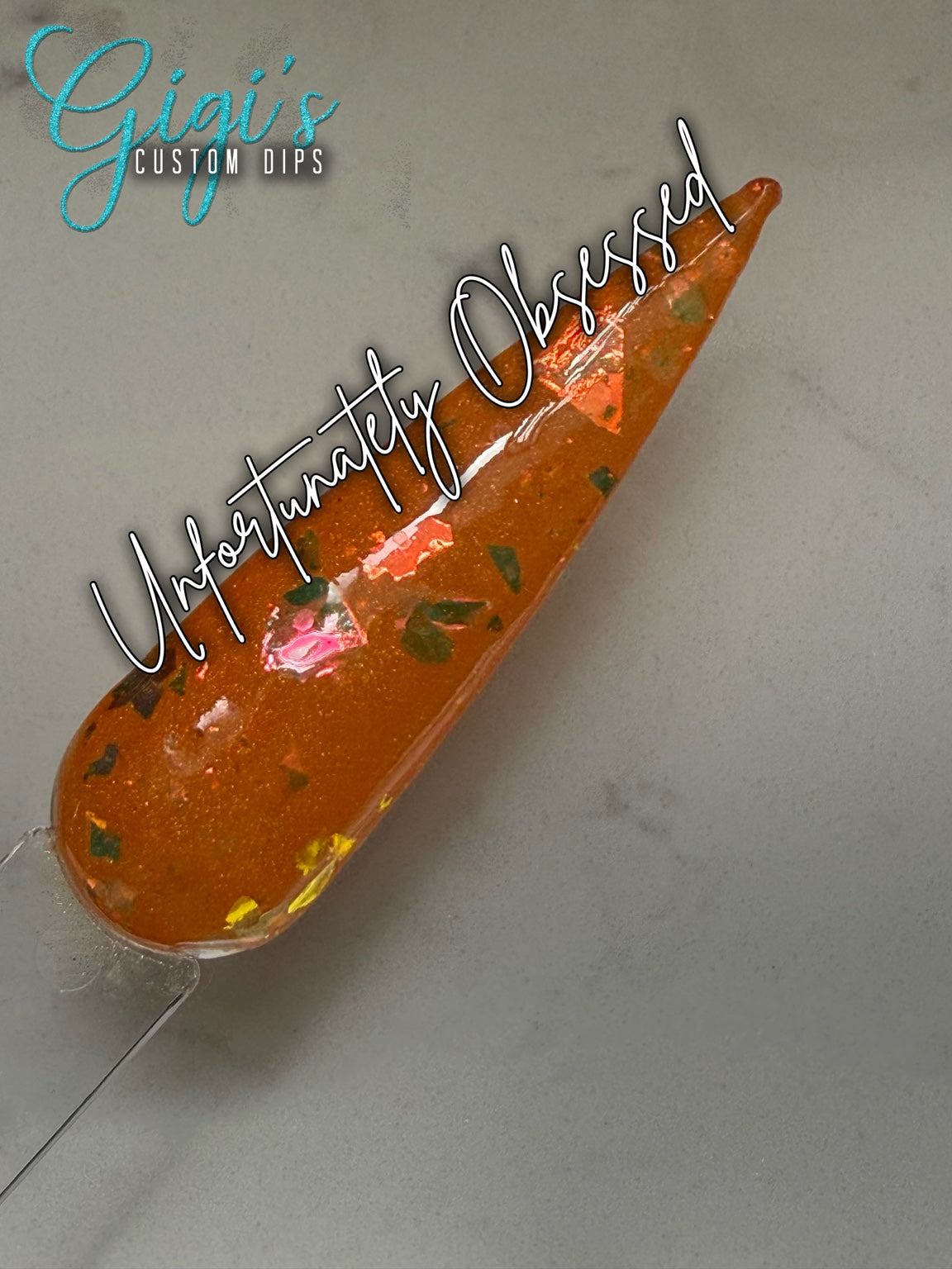Labeled Unfortunately Obsessed orange dip powder swatch with green, gold, bronze and pink colour-shifting flakes