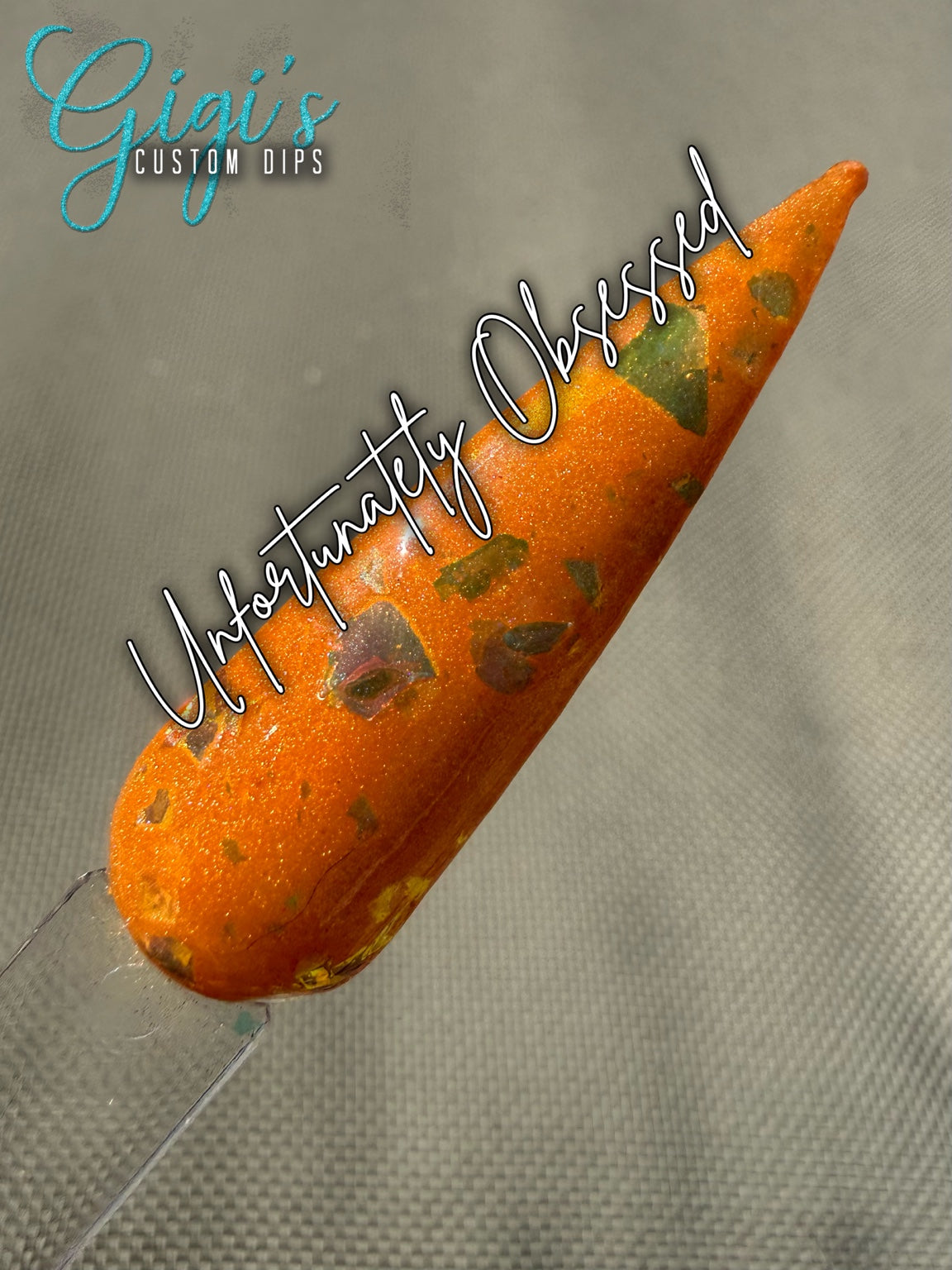 Labeled Unfortunately Obsessed orange dip powder swatch with green, gold, bronze and pink colour-shifting flakes